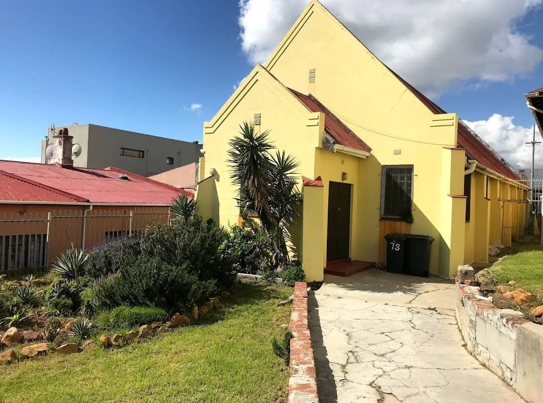The Ihsan Family Homes kitchen: a yellow gabled building at number 73, with a garden and paved path leading to the entrance.